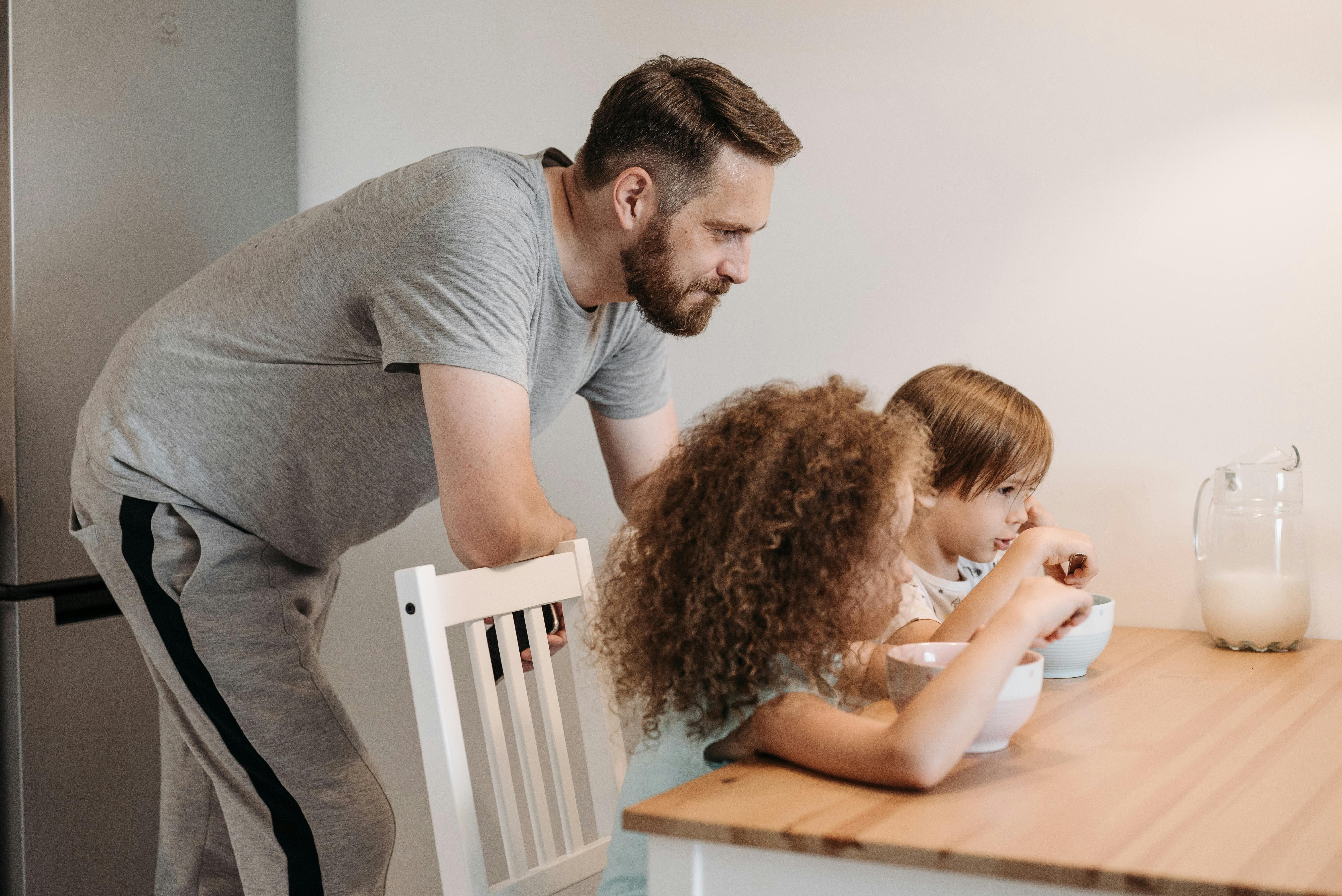A father watching his two girls eat breakfast | Source: Pexels